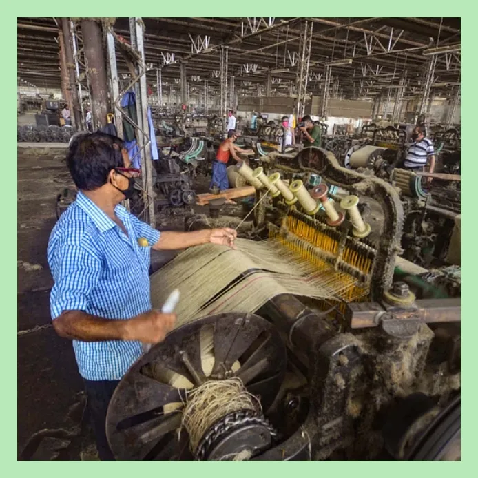 Worker operating jute weaving machine inside a busy jute mill.
