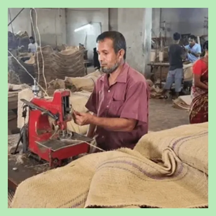 Worker stitching jute sacks using an industrial sewing machine in a jute bag production facility